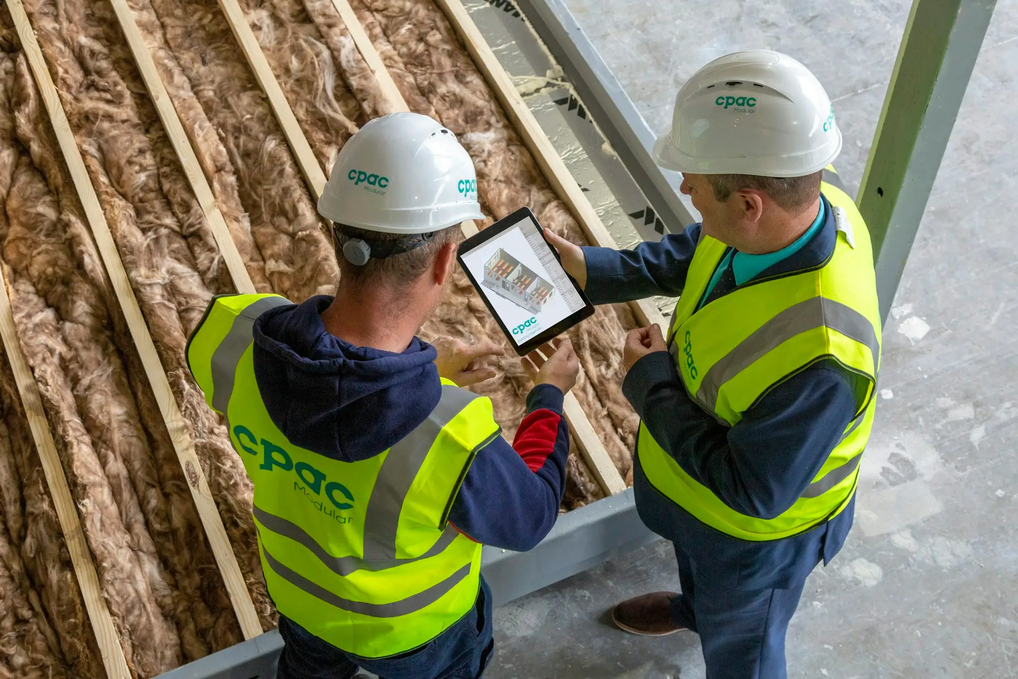 Builder in hi-vis reviewing a tax bill on a tablet beside a timber-framed house in Christchurch