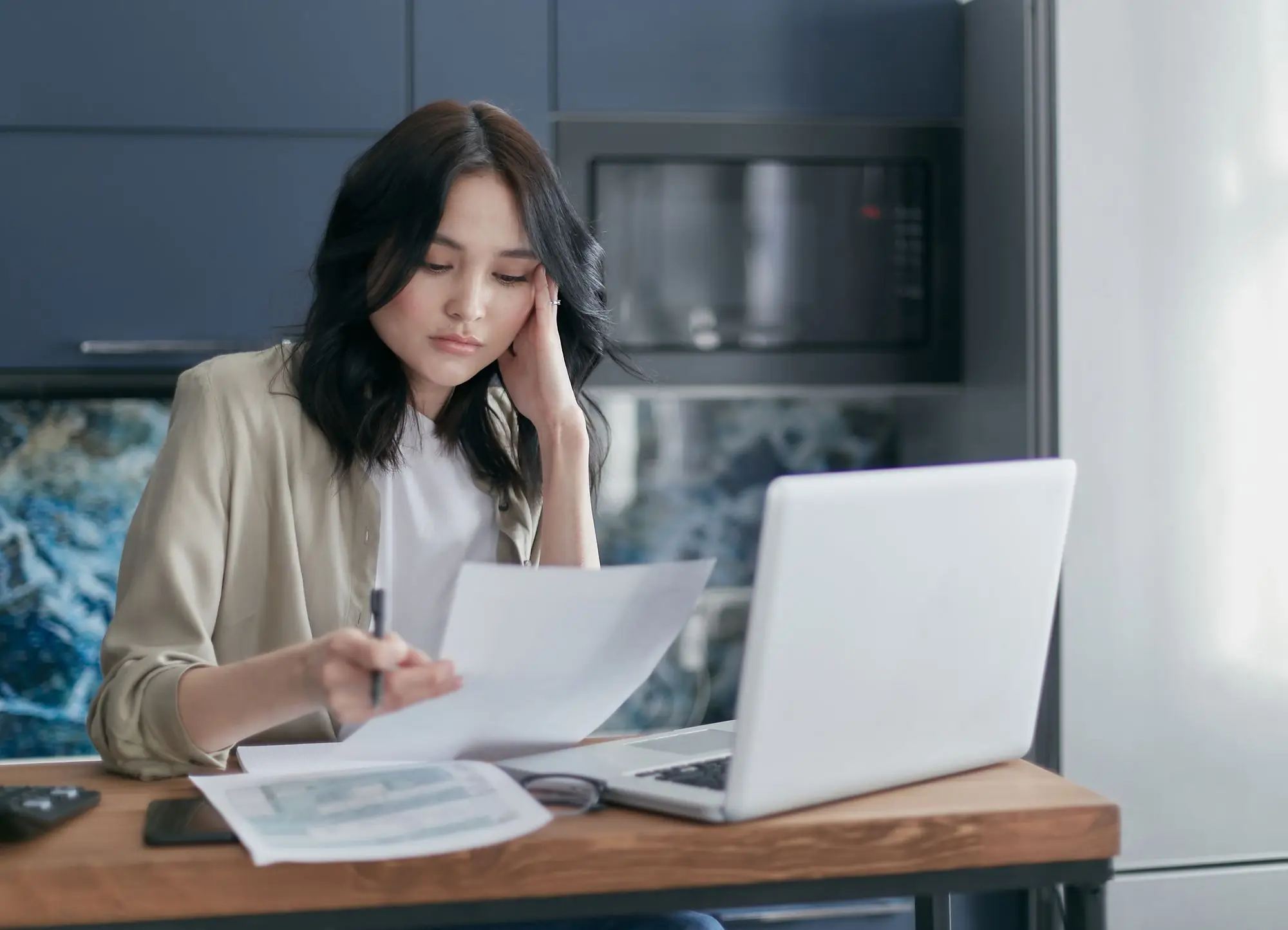 Business owner at her kitchen-office desk frowning over a printed letter about her company beside an open laptop