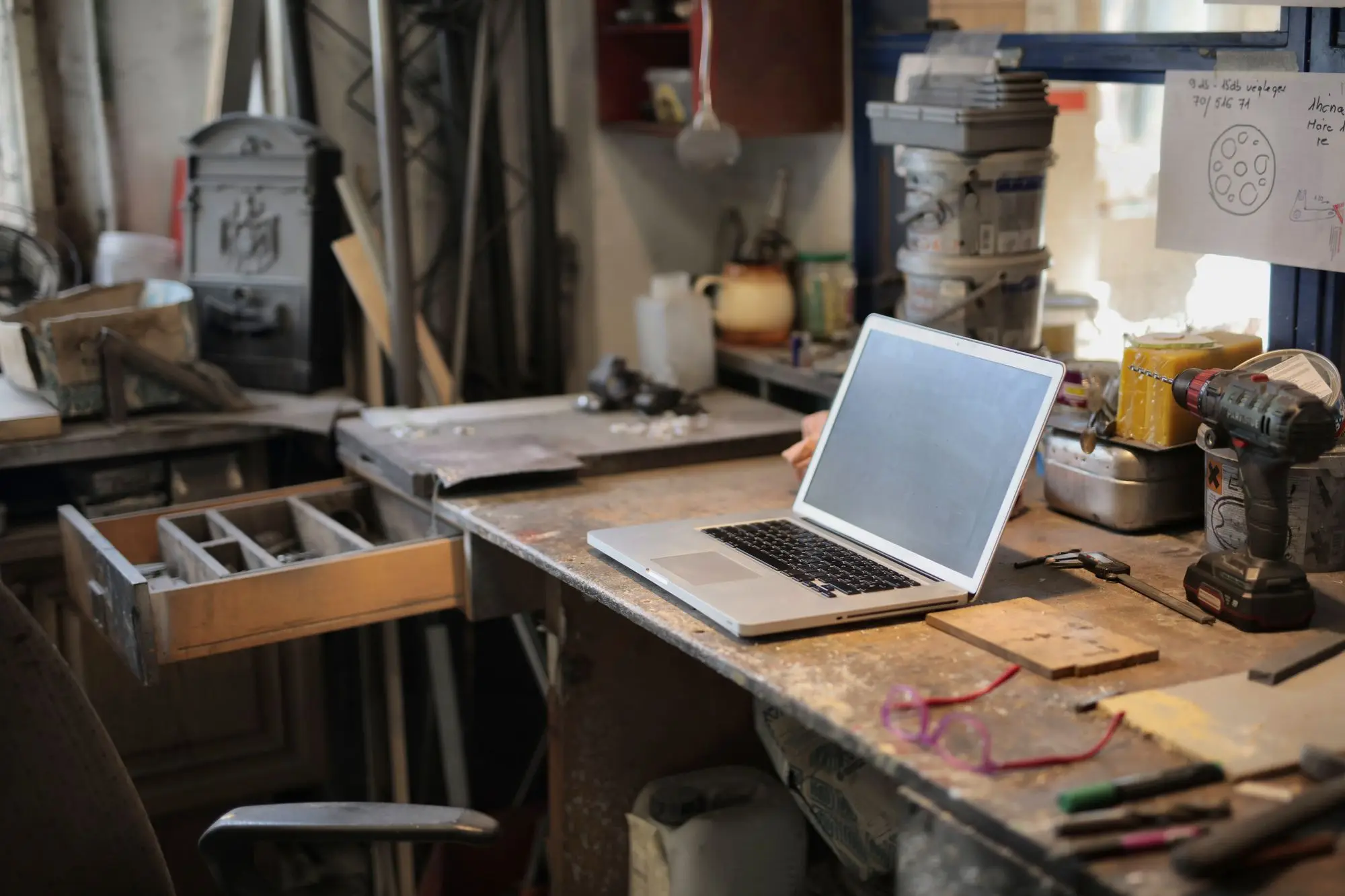 Laptop open on a small workshop bench among power tools, where the owner is working through a staff member’s final pay